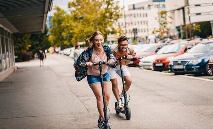 Zwei Personen fahren lachend auf E-Scootern